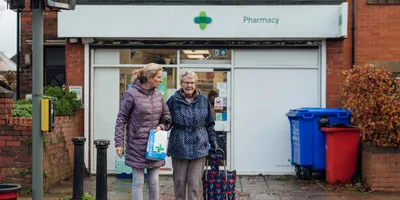 Two older women outside a UK pharmacy, picking up their prescriptions. 