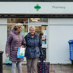 Two older women outside a UK pharmacy, picking up their prescriptions. 