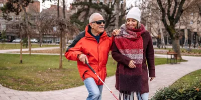 Young woman walking with blind, older man outside in the city public park