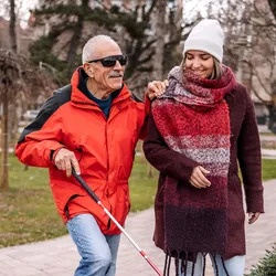 Young woman walking with blind, older man outside in the city public park