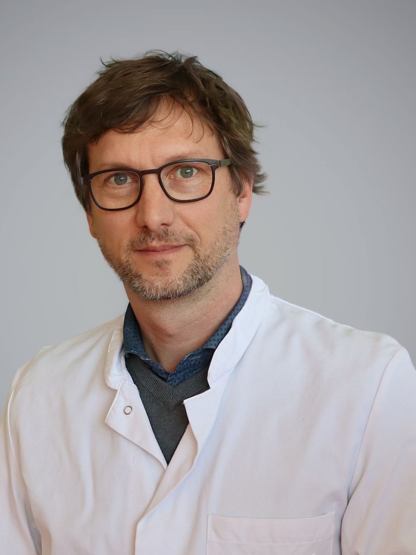 Martin Metz wears a white lab coat and smiles wearing glasses.