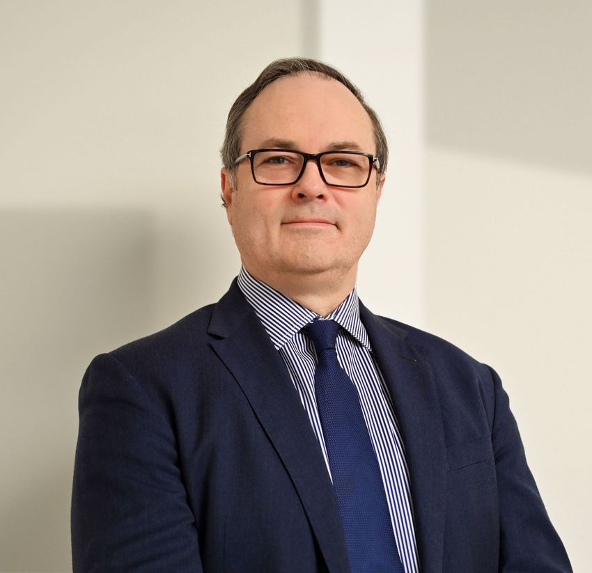 Craig Eagle wears glasses and a navy suit on a white background.