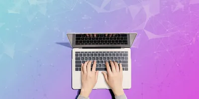 ands typing on an open laptop, viewed from above, against a colorful gradient background with abstract geometric network patterns.