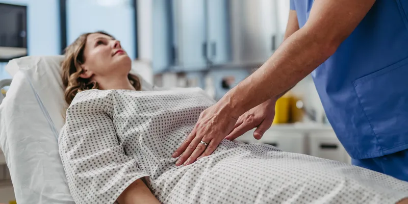 Doctor palpating woman's abdomen, using hands and steady pressure.