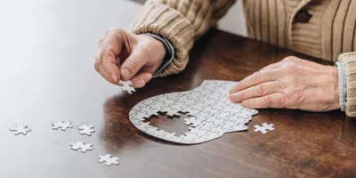 cropped view of senior man playing with a puzzle of a head, with part of the skull missing 