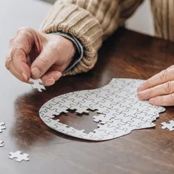 cropped view of senior man playing with a puzzle of a head, with part of the skull missing 