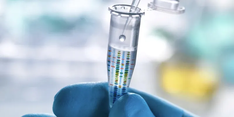 Gloved hand holding a microcentrifuge tube while a pipette dispenses liquid