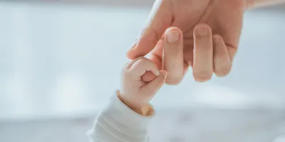 A baby holding the finger of an adult woman's hand