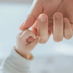 A baby holding the finger of an adult woman's hand