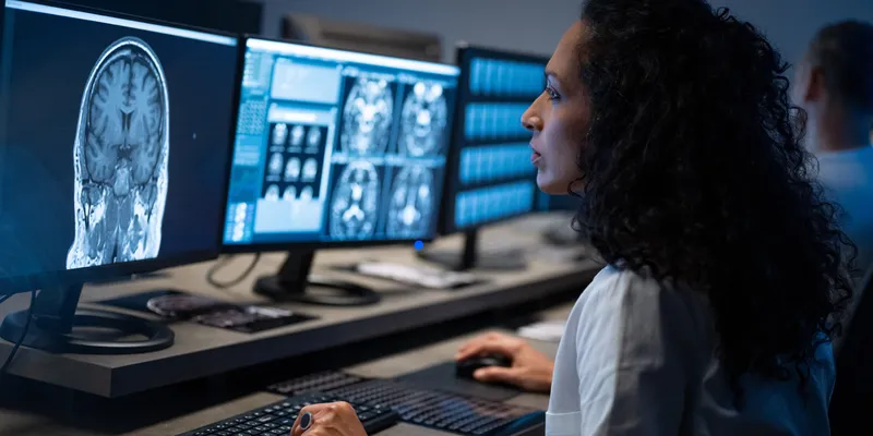 Side view of female radiologist looking at the MRI image of the head on her monitor and analyzing it.