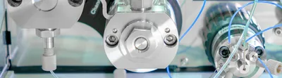 Binary pumps from an HPLC system are shown as three silver discs with blue and clear tubing against a clean laboratory background.