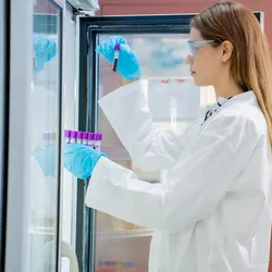A researcher in a lab coat retrieves labeled sample tubes from a laboratory freezer while examining a vial.