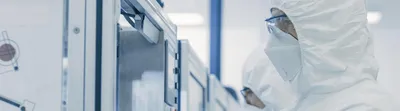 A cleanroom technician in full protective gear operates equipment in a sterile pharmaceutical manufacturing environment, illustrating aseptic processes and contamination control.
