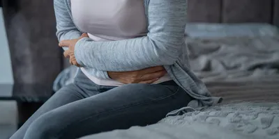 Woman clutching her stomach in pain while sitting on bed. 