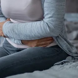 Woman clutching her stomach in pain while sitting on bed. 