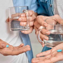 Two men holding a mug of water and a blue pill in their palms.