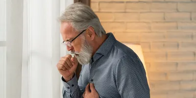 Photo of a man holding his chest and coughing into his hand