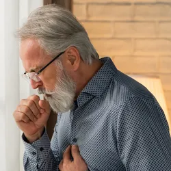 Photo of a man holding his chest and coughing into his hand