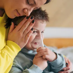 Mother taking care of her sick boy with an inhalation mask.