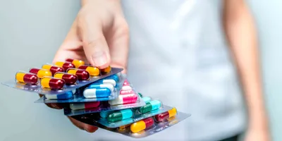 A hand holding four packets of colorful antibiotic pills