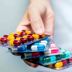 A hand holding four packets of colorful antibiotic pills