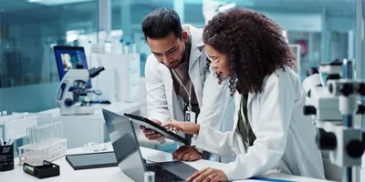 Two lab members looking at data on both a tablet and a laptop in a lab.