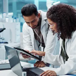 Two lab members looking at data on both a tablet and a laptop in a lab.