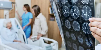 Elderly patient in hospital bed with a doctor holding onto images of MRI scans of the brain.