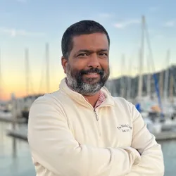 Headshot of Abhishek Jha, in front of some sailboats. 