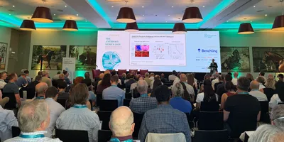 A back view of a crowded conference room with a large projector showing a science talk.
