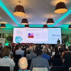 A back view of a crowded conference room with a large projector showing a science talk.