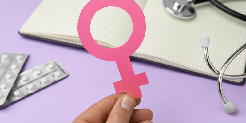 Girl holding female gender sign near open notebook, stethoscope, and blisters of pills on violet background.