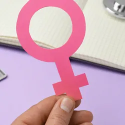 Girl holding female gender sign near open notebook, stethoscope, and blisters of pills on violet background.